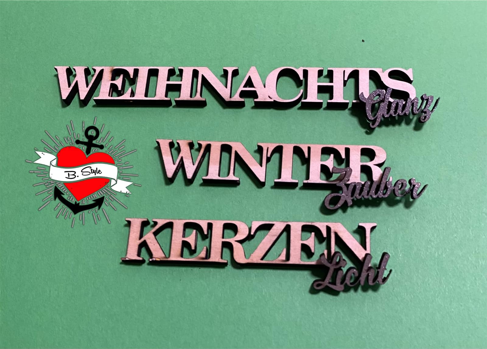 Kreative Holzbuchstaben von der Plotter Datei 'Weihnachtswörter Duo' von Easy-Sticks: Die stylischen Wörter 'WEIHNACHTS Glanz', 'WINTER Zauber' und 'KERZEN Licht' auf grünem Hintergrund, ideal für DIY-Projekte zur Weihnachtszeit.