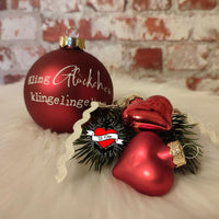 Rote Christbaumkugel mit der Aufschrift 'Kling Glückchen' zusammen mit roten Herzen und Tannenspitzen auf einem flauschigen Untergrund, von easy-sticks, Teil der Weihnachtsgrüße 2 Plotterdatei und PDF für Kerzengestaltung.
