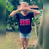 Eine Person im Freien, die die Augen mit den Händen verdeckt und ein schwarzes T-Shirt mit dem auffälligen Aufdruck "WEIRD" in Pink trägt, perfekt kombiniert mit der "Weird" Plotterdatei von easy-sticks.