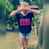 Eine Person im Freien, die die Augen mit den Händen verdeckt und ein schwarzes T-Shirt mit dem auffälligen Aufdruck "WEIRD" in Pink trägt, perfekt kombiniert mit der "Weird" Plotterdatei von easy-sticks.