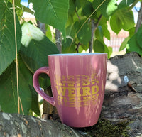 Eine stilvolle pinkfarbene Tasse mit dem Schriftzug "WEIRD" in Gold, platziert auf einem Baumstamm, ideal für kreative Projekte mit easy-sticks."Weird" Plotterdatei.