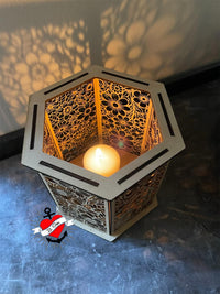 Das kreative Blumen Windlicht von easy-sticks, eine Laserdatei, zeigt eine hexagonale Form mit einem brennenden Teelicht. Die filigranen Blumenmuster sorgen für eine warme Atmosphäre, ideal für persönliche DIY-Projekte.