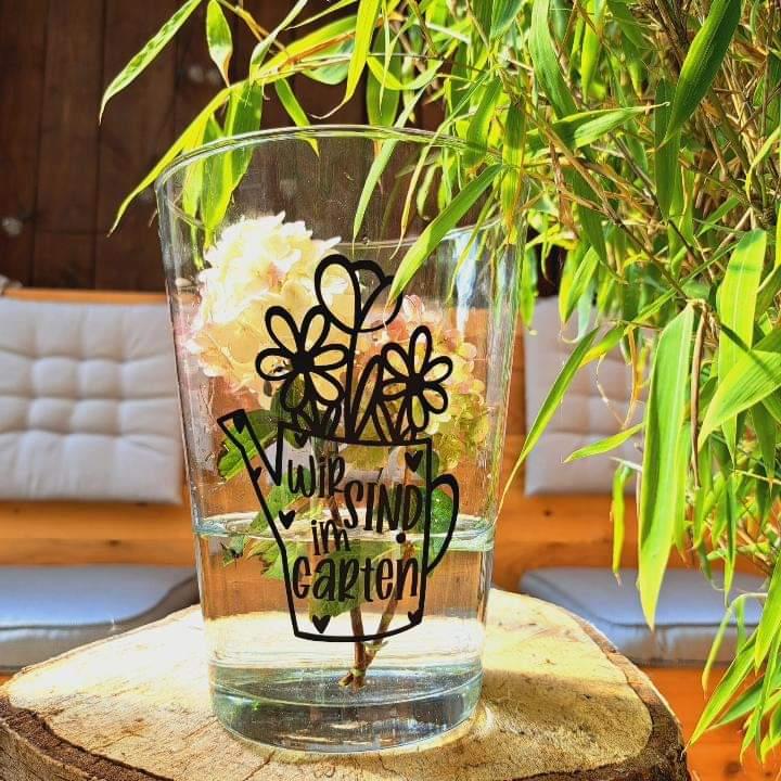 Kreative Plotterdatei Gießkanne "Wir Sind Im Garten" von easy-sticks, präsentiert auf einem Glas mit Blumen, ideal für Dekoideen im Garten.