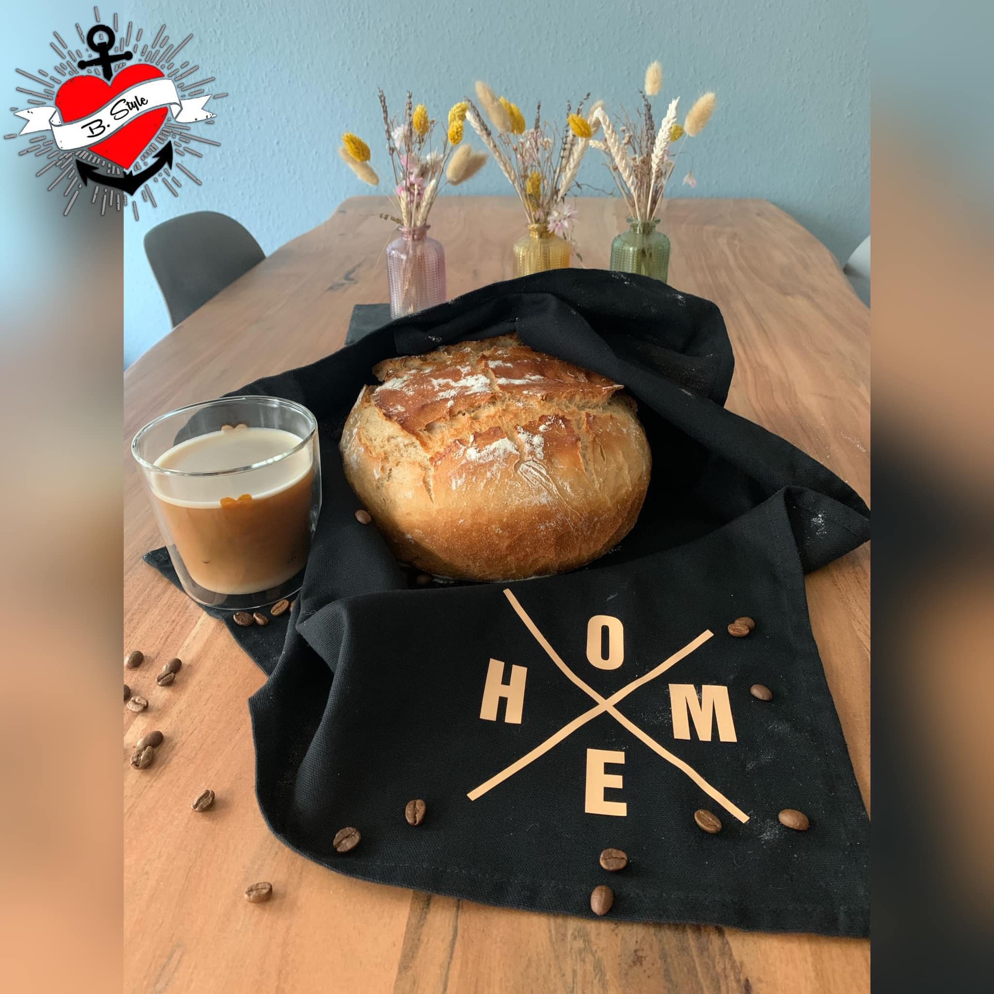 Ein frisch gebackenes Brot auf einem Tisch, umgeben von einer schwarzen Tischdecke mit dem Schriftzug "X Worte", gestaltet von easy-sticks.