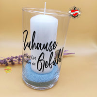 Eine stilvolle Glaslaterne mit der Aufschrift 'Zuhause ist kein Ort, sondern ein Gefühl' von easy-sticks, dekoriert mit farbigen Sand und Lavendelblüten.