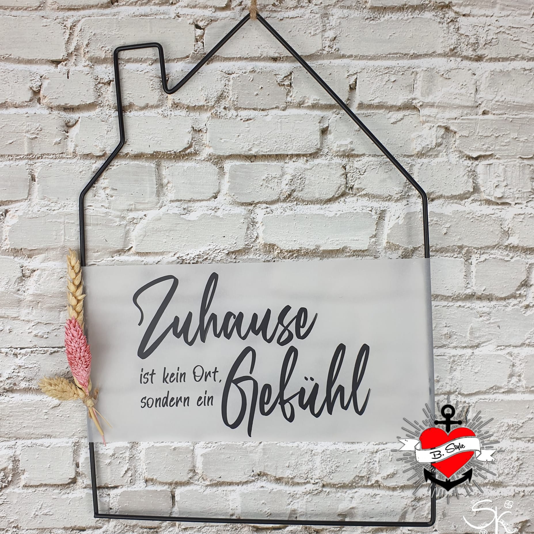 Eine elegante Deko in Form eines Hauses mit dem Spruch 'Zuhause ist kein Ort, sondern ein Gefühl' von easy-sticks, auf einem rustikalen Backstein Hintergrund.