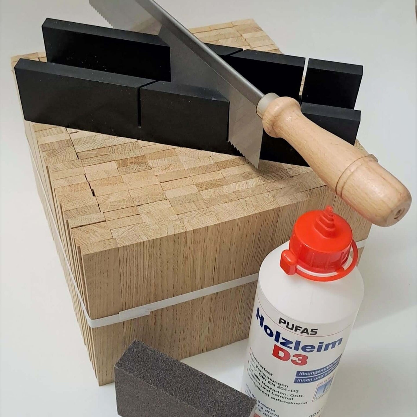Easy-Sticks 4.0 Starter Set von Easy-Sticks mit Säge, Holzleim und Schleifschwamm auf einem stabilen Holzblock. Ideal für kreative Bastelprojekte und DIY-Anwendungen.