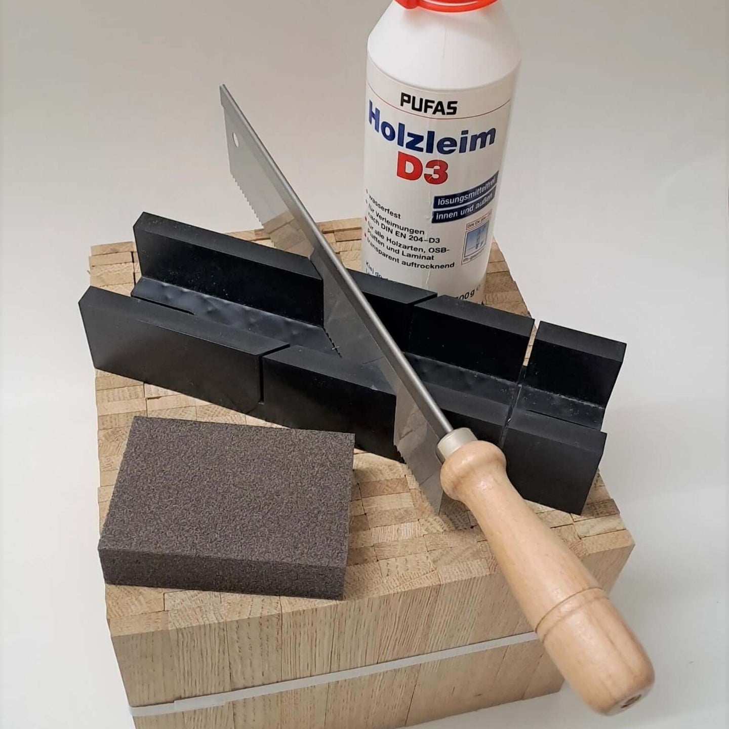 Easy-Sticks 4.0 Starter Set von Easy-Sticks präsentiert mit Säge, Holzleim und Schleifschwamm auf einem robusten Holzblock. Perfekt für Modelle und Bastelarbeiten.