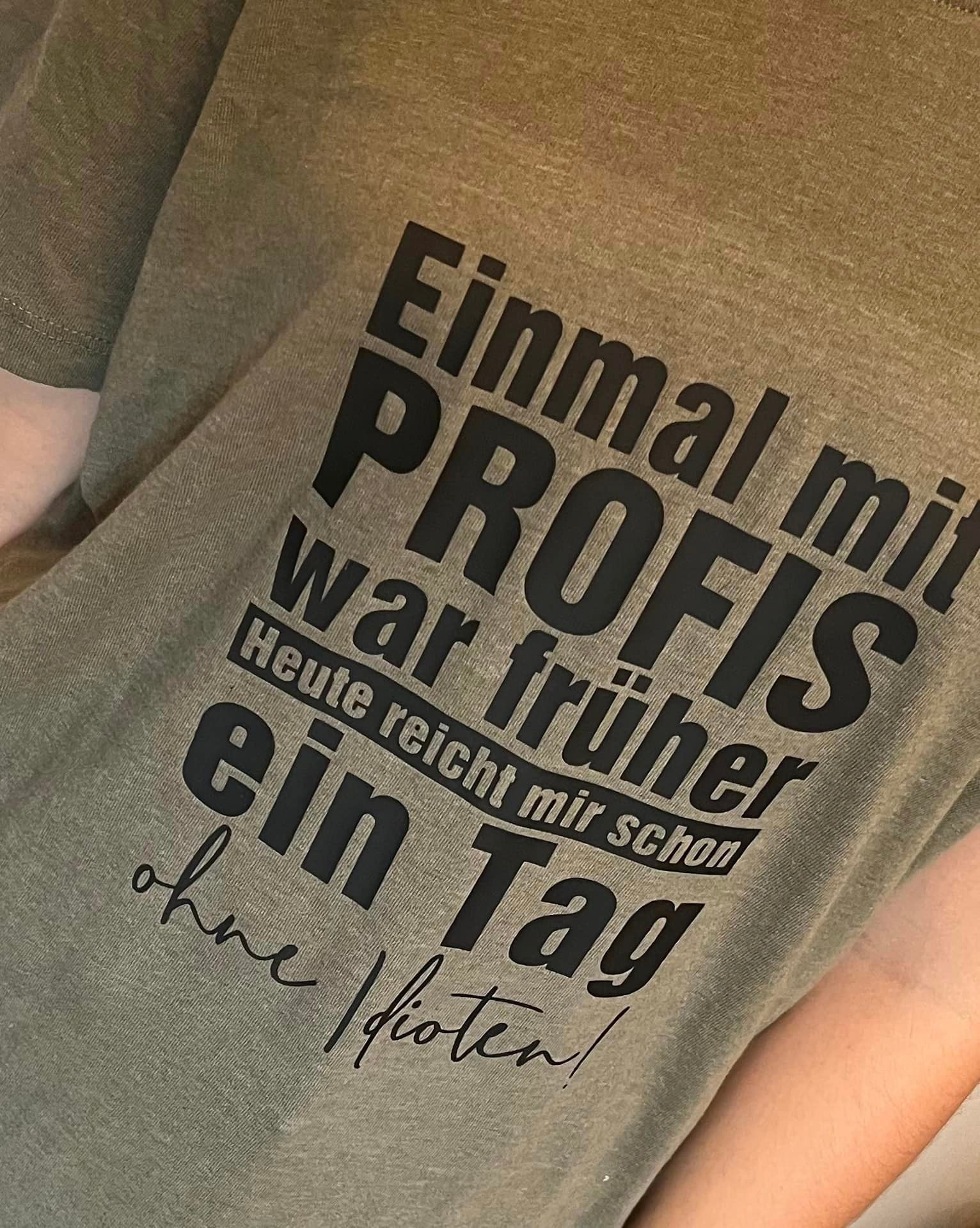 Nahaufnahme eines T-Shirts in olivgrün mit dem Aufdruck "Einmal mit PROFIS war früher Heute reicht mir schon ein Tag ohne Idioten!" von easy-sticks, ideal für kreative DIY-Ideen.