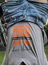 Detailaufnahme eines grauen T-Shirts mit dem Spruch "Einmal mit PROFIS war früher Heute reicht mir schon ein Tag ohne Idioten!" in orange von easy-sticks, ideal für persönliche Gestaltung.