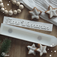 Verschiedene Silikonformen von Easy-Sticks, darunter 'Frohe Weihnachten', dekoriert mit winterlichen Plätzchen und festlicher Dekoration.