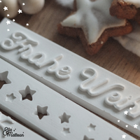 Detailansicht der Easy-Sticks Silikonformen in Weiß mit 'Frohe Weihnachten' und weihnachtlichen Sternen, ideal für DIY Weihnachtsdekoration.