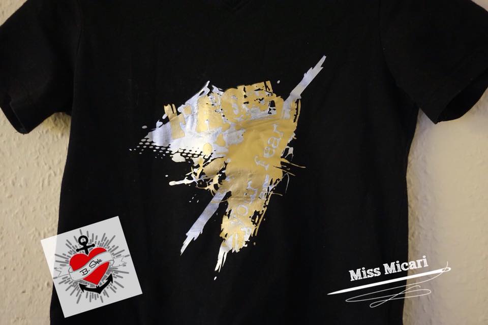 Stylisches T-Shirt mit dem grafischen Design "Face your fear" von Easy-Sticks in Silber und Gold auf schwarzem Hintergrund, ideal für kreative Projekte.