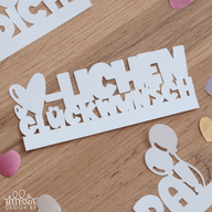 Weißer Kartenausschnitt mit der Plotterdatei 'HERZLICHEN GLÜCKWUNSCH' von easy-sticks auf einem Holztisch. Ideal für kreative Geschenke und individuelle Karten.