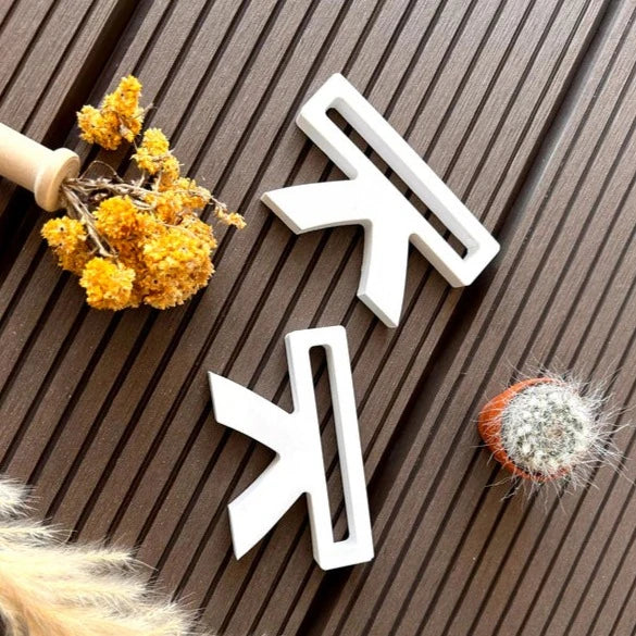 Zwei weiße Silikonformen von Easy-Sticks, ideal zum Basteln von dekorativen Sitzbänken, auf einer Holzoberfläche mit gelben Blumen und einer kleinen Kaktus-Dekoration.