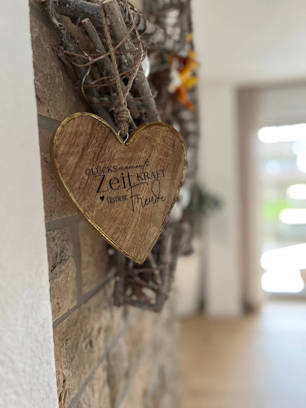 Herzförmiger Dekorationsanhänger mit der Aufschrift "Glücks Momente Zeit Kraft Freude", dekorativ an einer Steinwand hängend. Perfekt für kreative DIY Projekte mit den Rub On UV Stickern von easy-sticks, die Gestaltung und Individualisierung erleichtern.