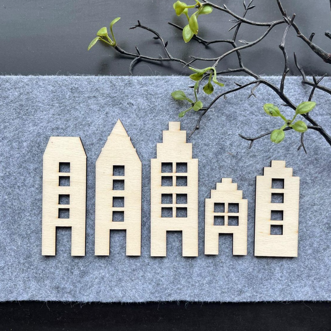 Fein gestaltete Holzhäuser in verschiedenen Formen auf grauem Filz, ideal für kreative DIY Projekte. Häusermotive zum Downloaden von easy-sticks.