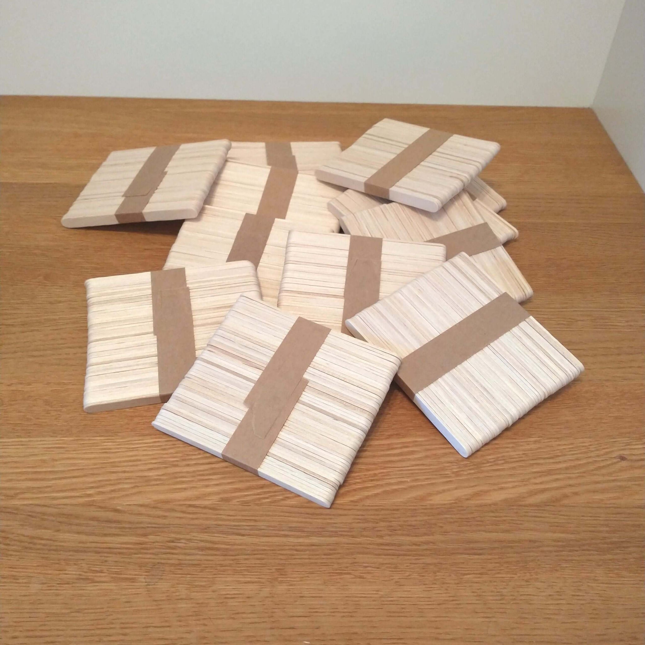 Kreative Anordnung der Easy-Sticks Ice von Easy-Sticks: Mehrere Pakete dünner Bastelsticks aus Holz, ideal für DIY-Projekte auf einem Holztisch.