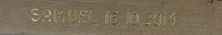 Nahaufnahme der Goldbuchstaben "SAMUEL 16.10.2014" auf Holz von easy-sticks, eine stilvolle personalisierte Beschriftung.