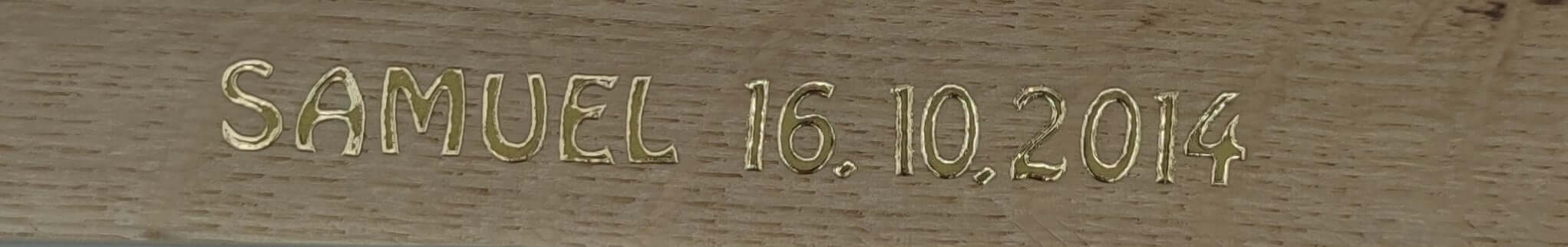 Nahaufnahme der Goldbuchstaben "SAMUEL 16.10.2014" auf Holz von easy-sticks, eine stilvolle personalisierte Beschriftung.