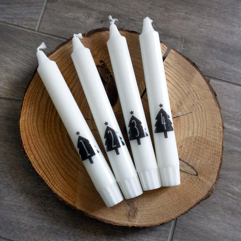 Vier dekorierte Weihnachtskerzen mit Baum-Motiven auf einem Holzuntergrund, perfekt für gemütliche Weihnachtsstimmung, von easy-sticks, Weihnachtskerzen Sticker PDF Download für Stabkerzen mit festlichen Motiven.